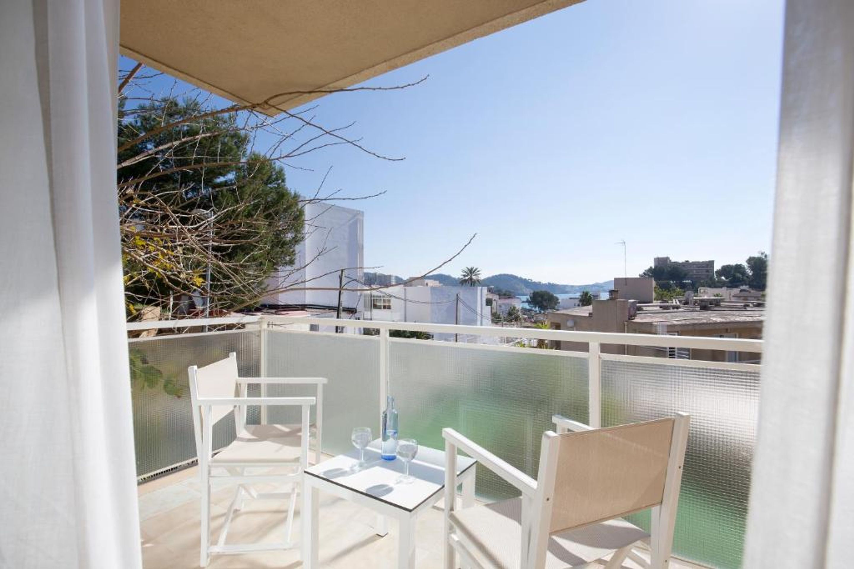 A balcony with a table and chairs, overlooking a body of water and buildings.