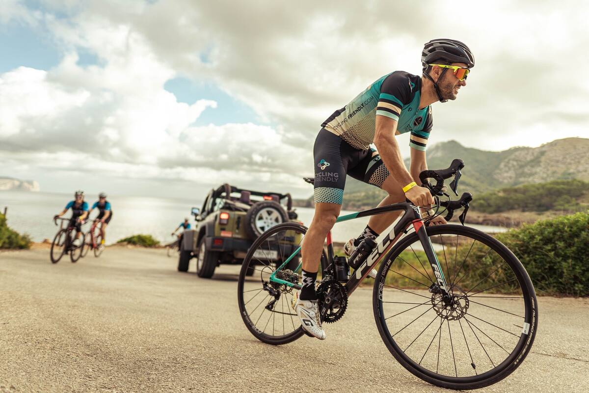 A cyclist on a road with a vehicle and another cyclist in the background.