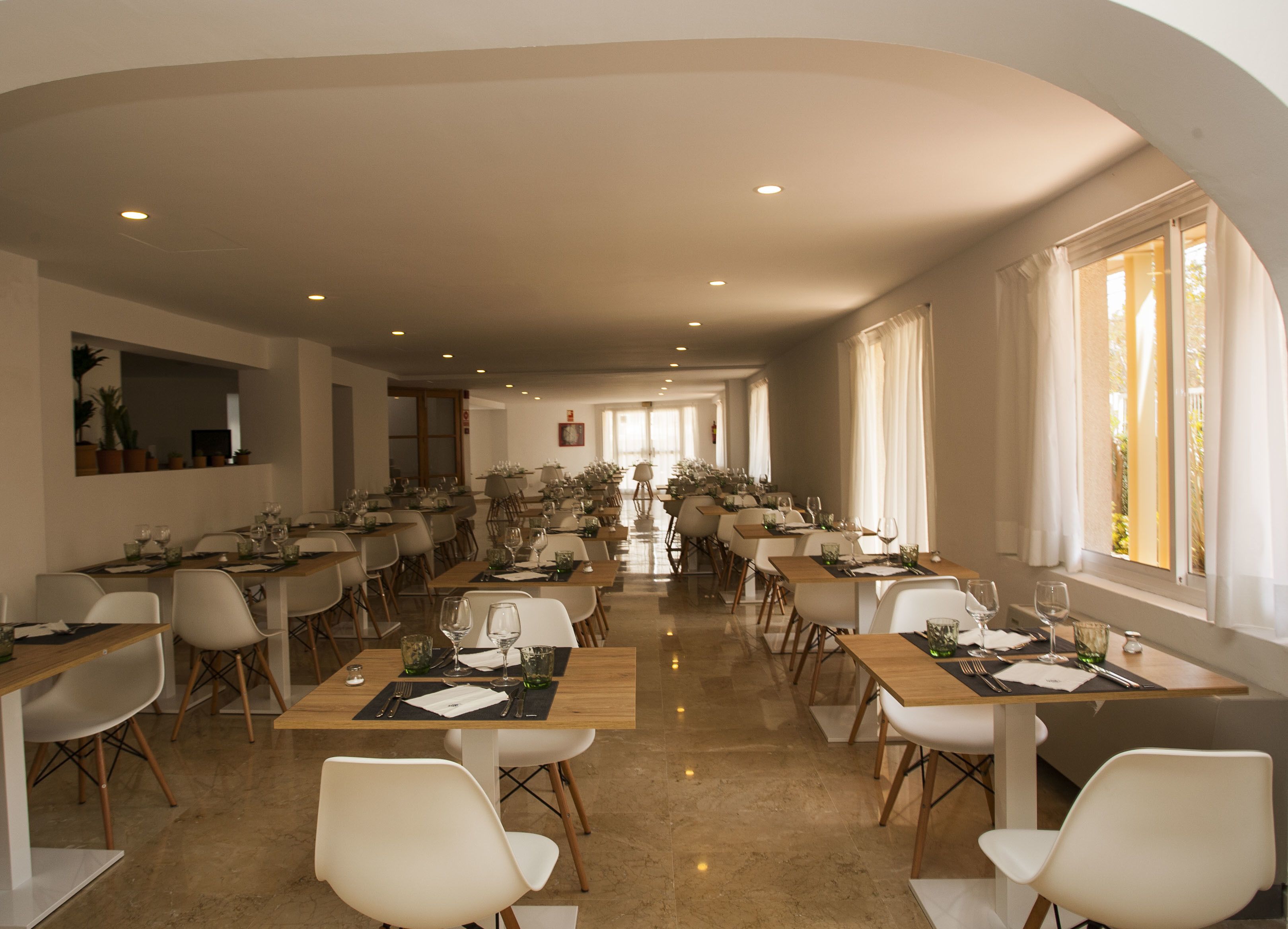 Un comedor amplio con múltiples mesas y sillas, ventanas grandes con cortinas, y un diseño de interiores moderno.