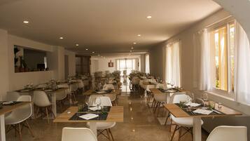 Un comedor amplio con múltiples mesas y sillas, ventanas grandes con cortinas, y un diseño de interiores moderno.