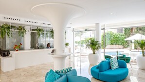 Rebuda moderna amb taulell de recepció, zona de seients i grans finestres que donen vistes a la zona de la piscina exterior.