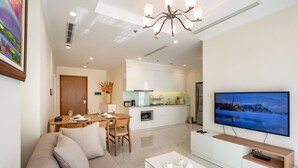 Ein modernes Wohnzimmer mit Sofa, Couchtisch und Fernseher. Es gibt einen Essbereich mit Tisch und Stühlen sowie eine Küche mit weißen Schränken und einem Herd.