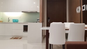 Eine moderne Küche mit weißen Schränken, einer zentralen Kochinsel und einem Essbereich mit weißen Stühlen und einem braunen Sofa.