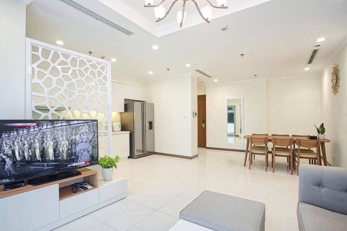 Una sala de estar moderna con televisor de pantalla plana, un comedor con sillas de madera y una cocina con refrigerador.