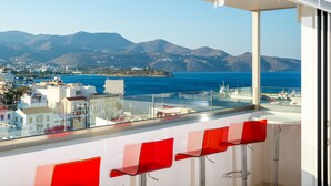 Een balkon met rode stoelen, een helder uitzicht op zee en gebouwen op de achtergrond.