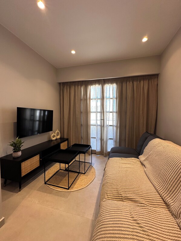 Una sala moderna con un televisor de pantalla plana, un sofá, una mesa de centro y una mesa de comedor.