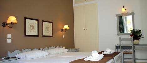 Habitación de hotel con dos camas, un escritorio y una silla. Se observan cuadros enmarcados en la pared, un espejo y una planta en maceta.