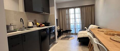 A modern kitchen with dark cabinets, a dishwasher, and a stove. There is a dining area with a wooden table and chairs.
