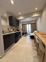 Una cocina moderna con armarios oscuros, lavavajillas y estufa. Hay una zona de comedor con mesa y sillas de madera.