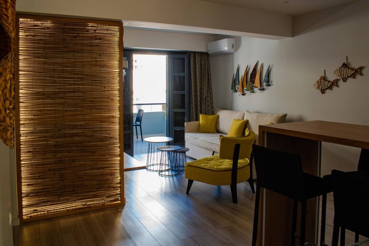 Una sala moderna con sofá, sillones amarillos, una mesa de comedor y un balcón con vistas.