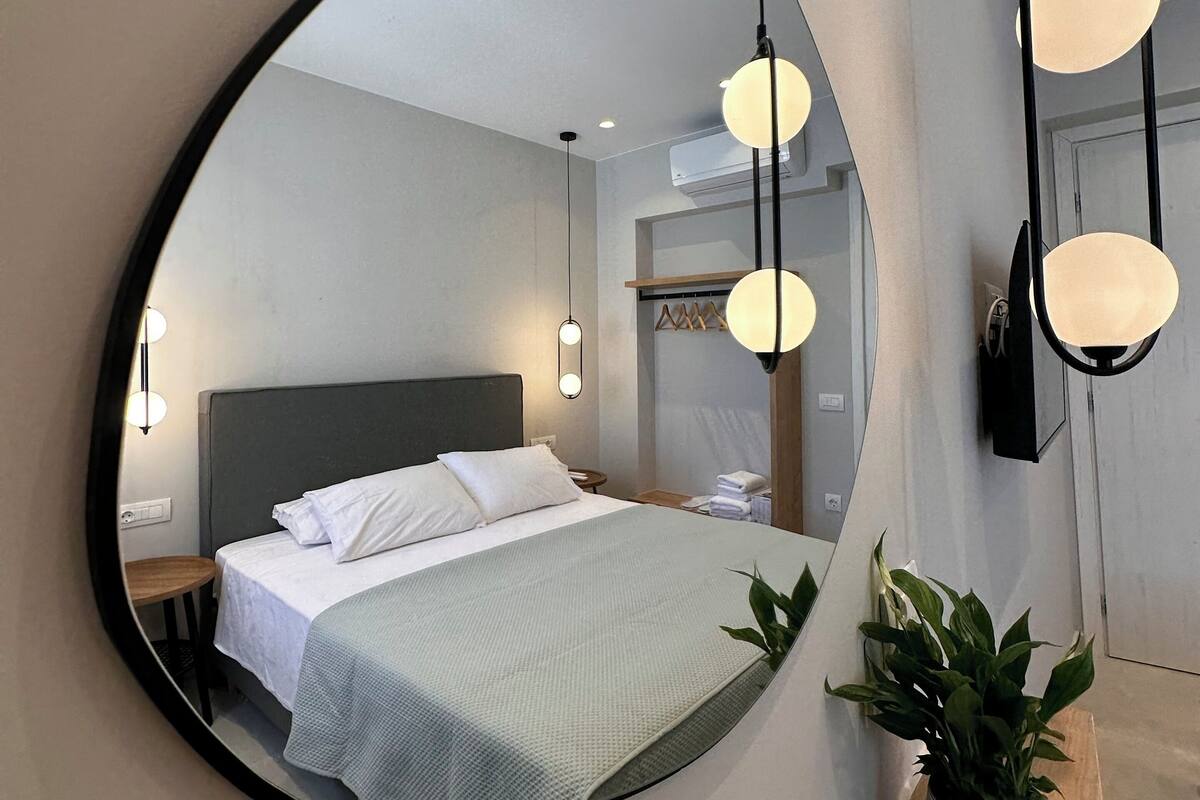 Un dormitorio con un espejo grande, una cama, mesitas de noche y una planta en maceta.