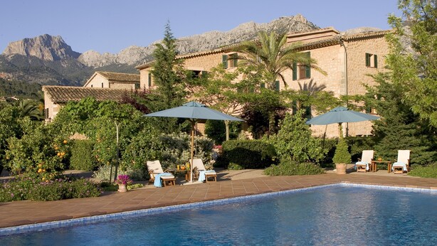 Una piscina con lettini e ombrelloni, circondata da vegetazione rigogliosa e con le montagne sullo sfondo.
