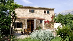 Un edificio in pietra con una porta di legno, un piccolo patio con tavolo e sedie, e un giardino con diverse piante.