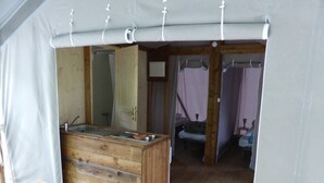 A tented room with a wooden bench, a sink, and a bed with a canopy. - Camping Les Vignes (Puy-l'Eveque)