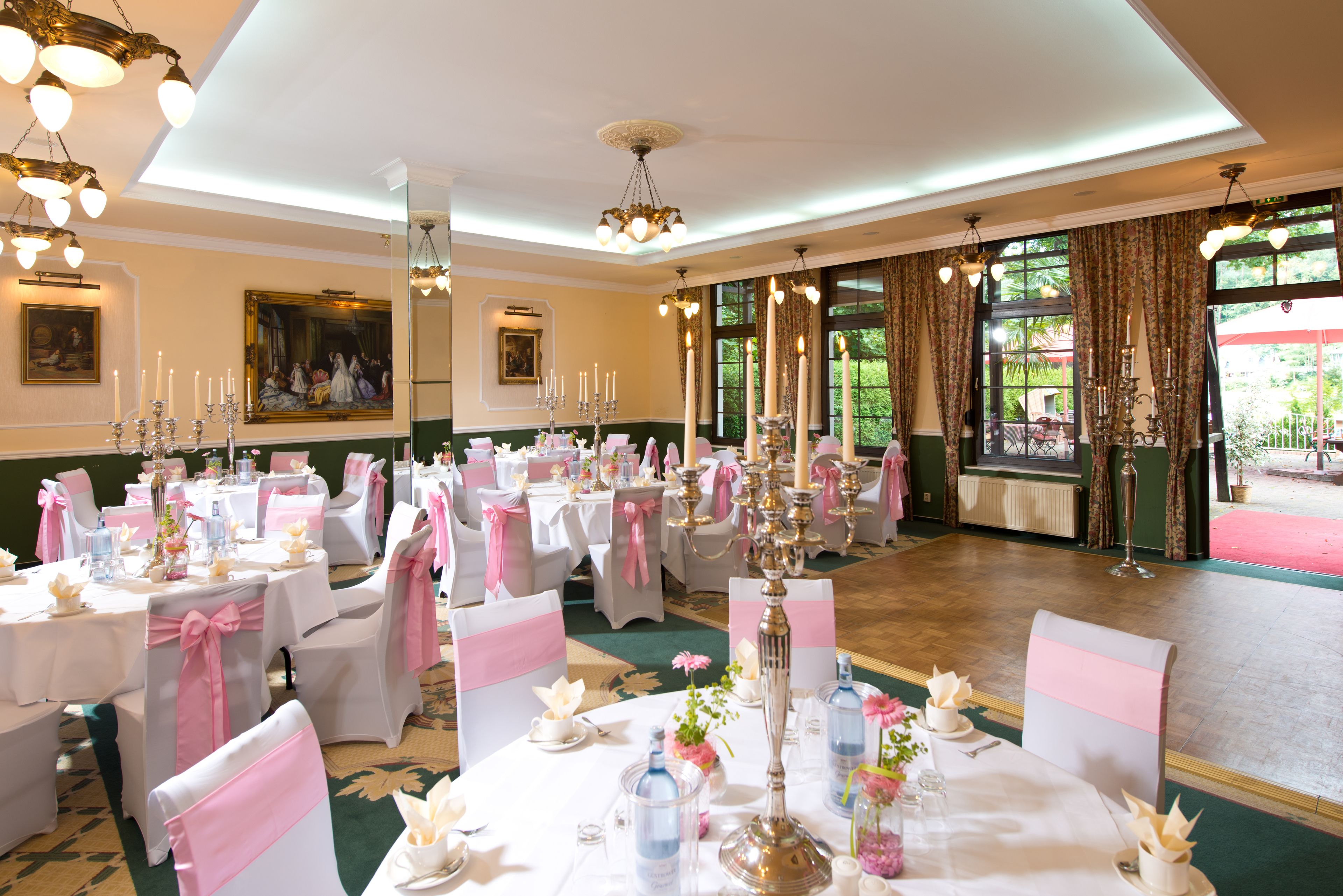 Un salón de banquetes con mesas redondas, sillas blancas y rosas, y candelabros.