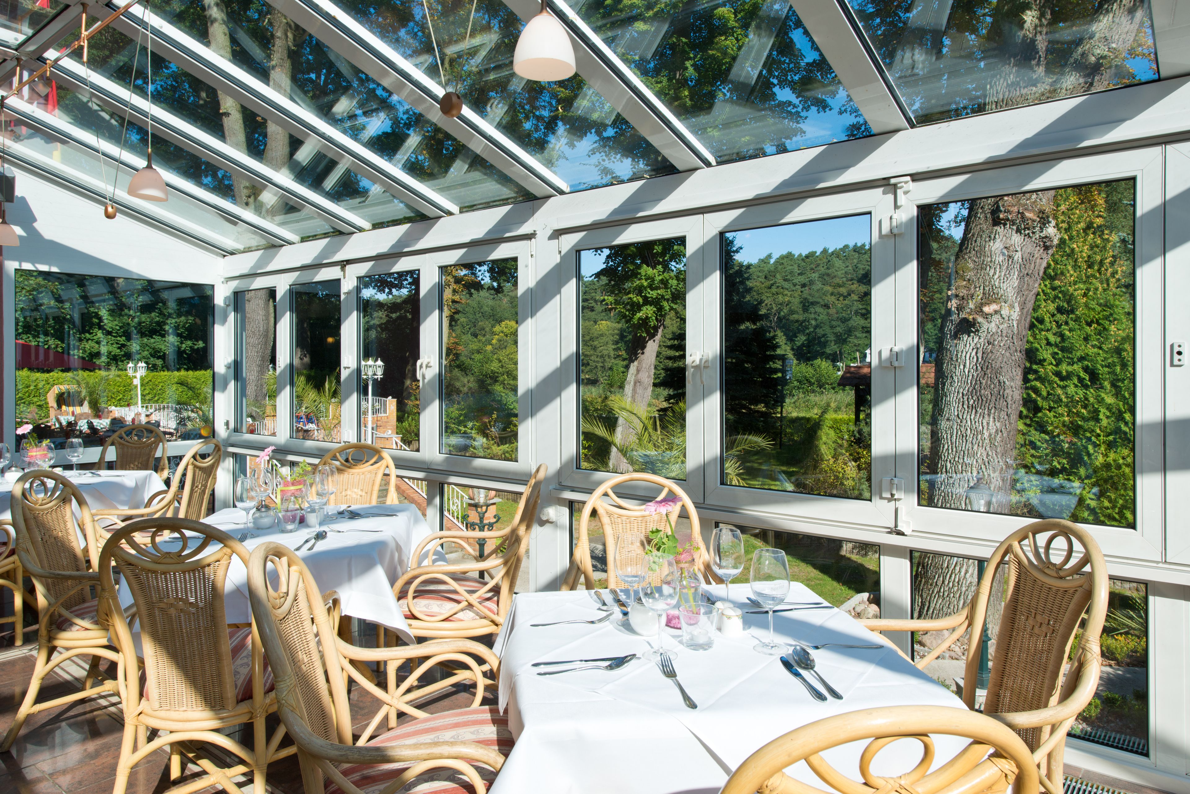 Un restaurante con paredes de vidrio, muebles de mimbre y manteles blancos.