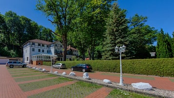 A paved pathway with a row of white bollards, a building with a traditional facade, and a hedge in the background.