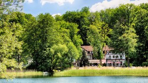 A lakeside hotel with a traditional European architectural style, featuring a prominent building with a tiled roof and a balcony.