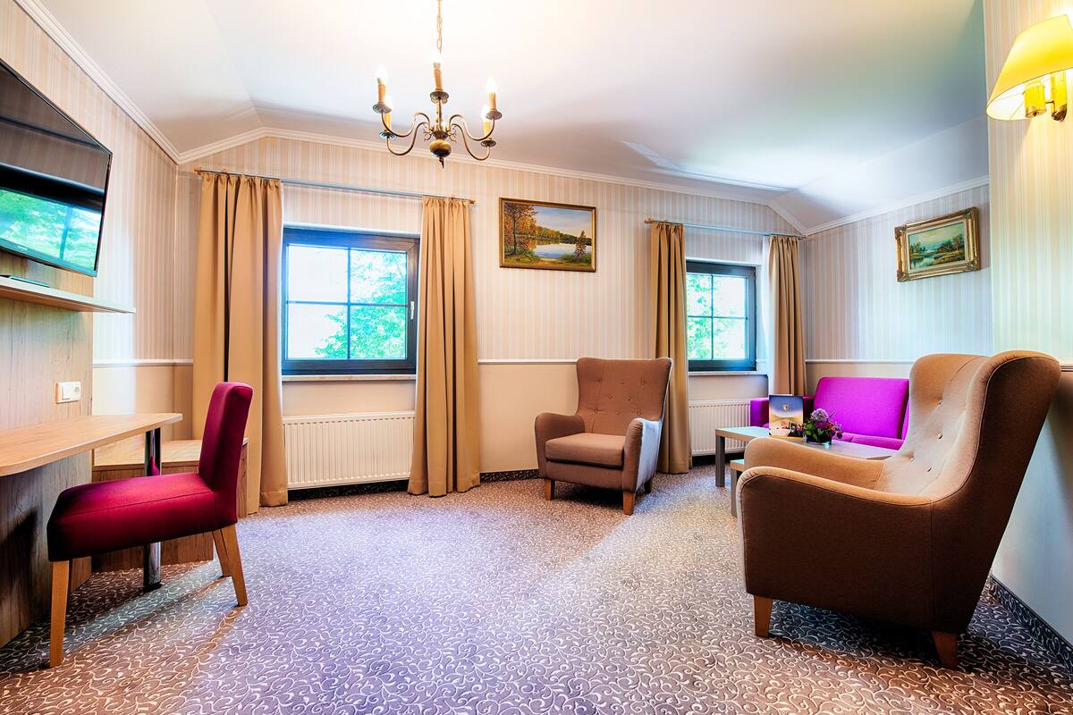 Habitación de hotel con un escritorio de madera, dos sillones, un sofá, un televisor y una araña.