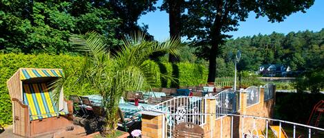 A patio area with outdoor seating, a small table with a vase, and a view of a forested area.