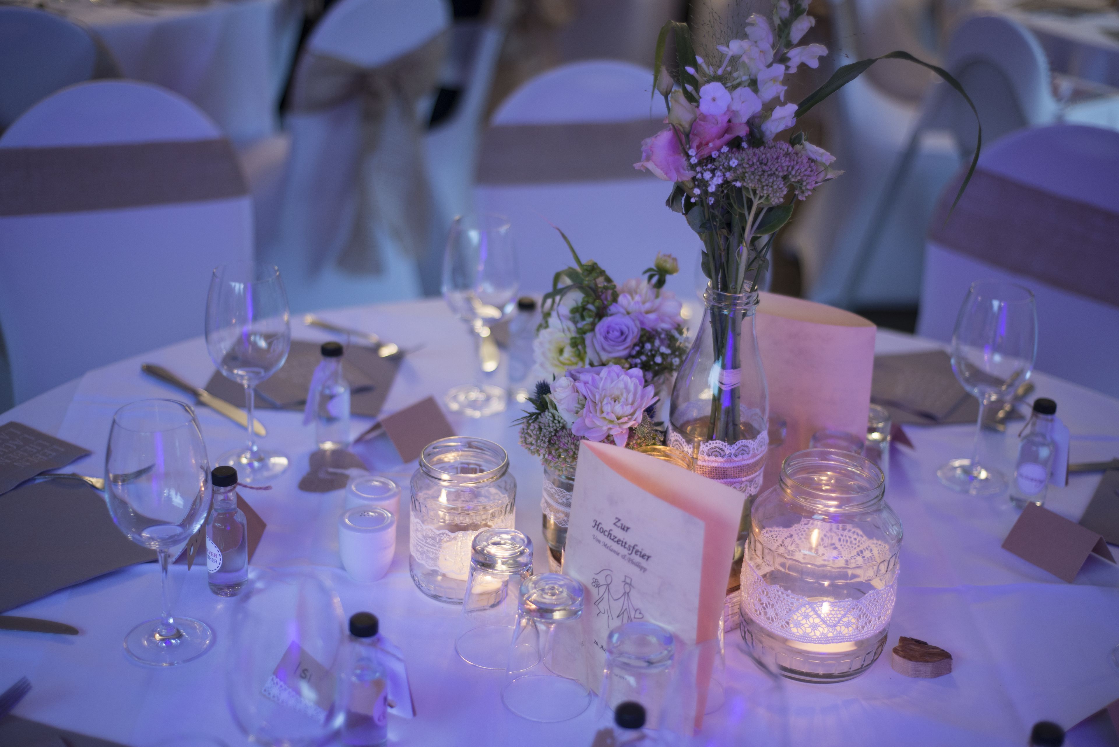 Een gedekte tafel voor een formeel evenement, met glaswerk, kaarsen en bloemstukken.