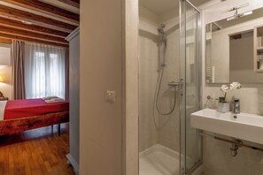 Een hotelkamer met een bed, een douche en een badkamer met een wastafel en spiegel.