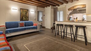 A living room with a sofa, a kitchen area with stools, and a wooden ceiling. - Biennale Garden Art & Architecture Venue (Venice)