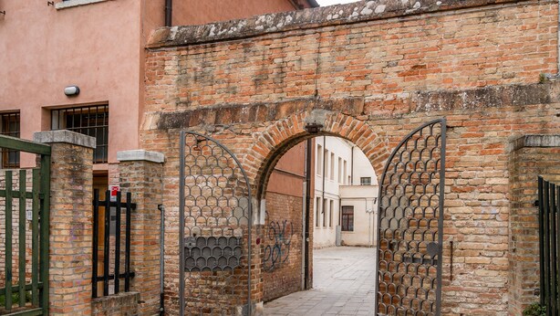 An arched brick gate with metal bars, leading to a narrow alleyway. - Biennale Garden Art & Architecture Venue (Venice)