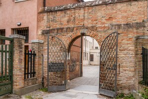 Een gebogen bakstenen poort met metalen tralies, die leidt naar een smalle steeg.