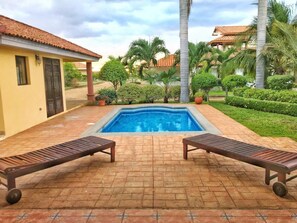 A swimming pool with two lounge chairs, surrounded by palm trees and a well-maintained garden. - Casa Carolina Gran Pacifica Resort (Villa El Carmen)