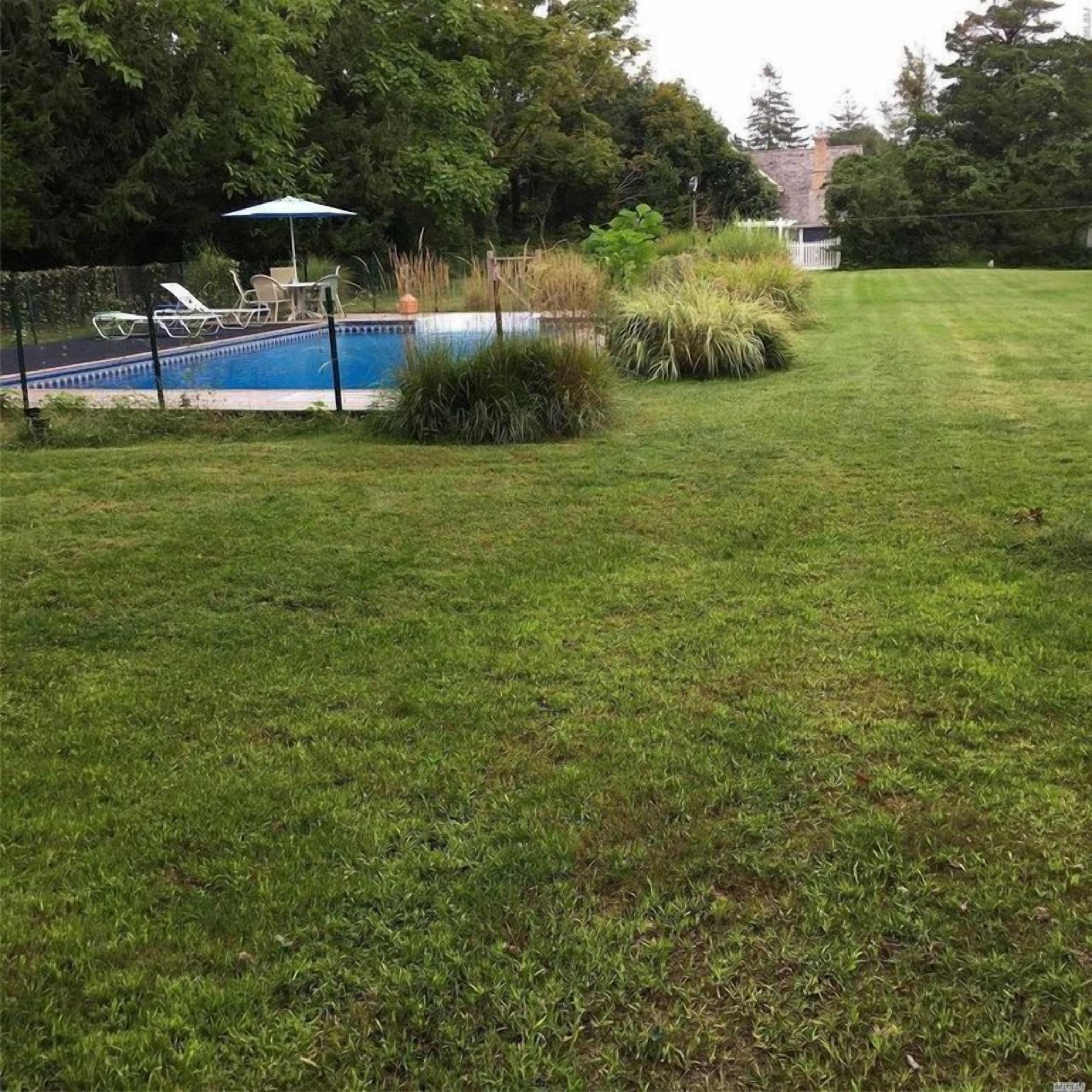 Ein Garten mit Schwimmbecken, Rasen und weißem Zaun.