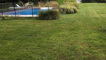 Ein Garten mit Schwimmbecken, Rasen und weißem Zaun.