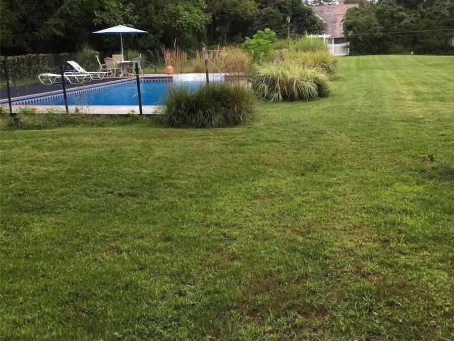 Ein Garten mit Schwimmbecken, Rasen und weißem Zaun.
