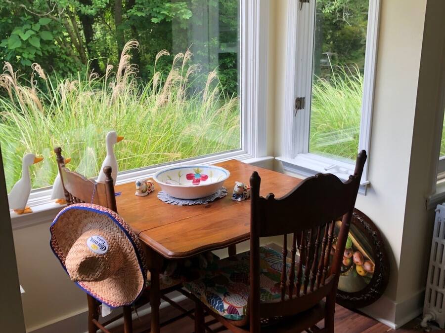 A dining area with a wooden table, chairs, and a view of greenery through large windows.