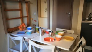 Una mesa de comedor con diferentes recipientes y un jarrón con flores. Hay sillas alrededor de la mesa y un mueble en el fondo.