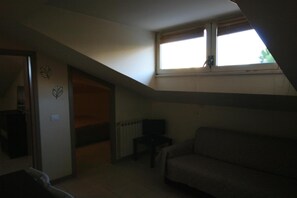 A dimly lit room with a sloped ceiling, a radiator, a sofa, and a small table. - Casa vacanze Cucciolo (Rimini)