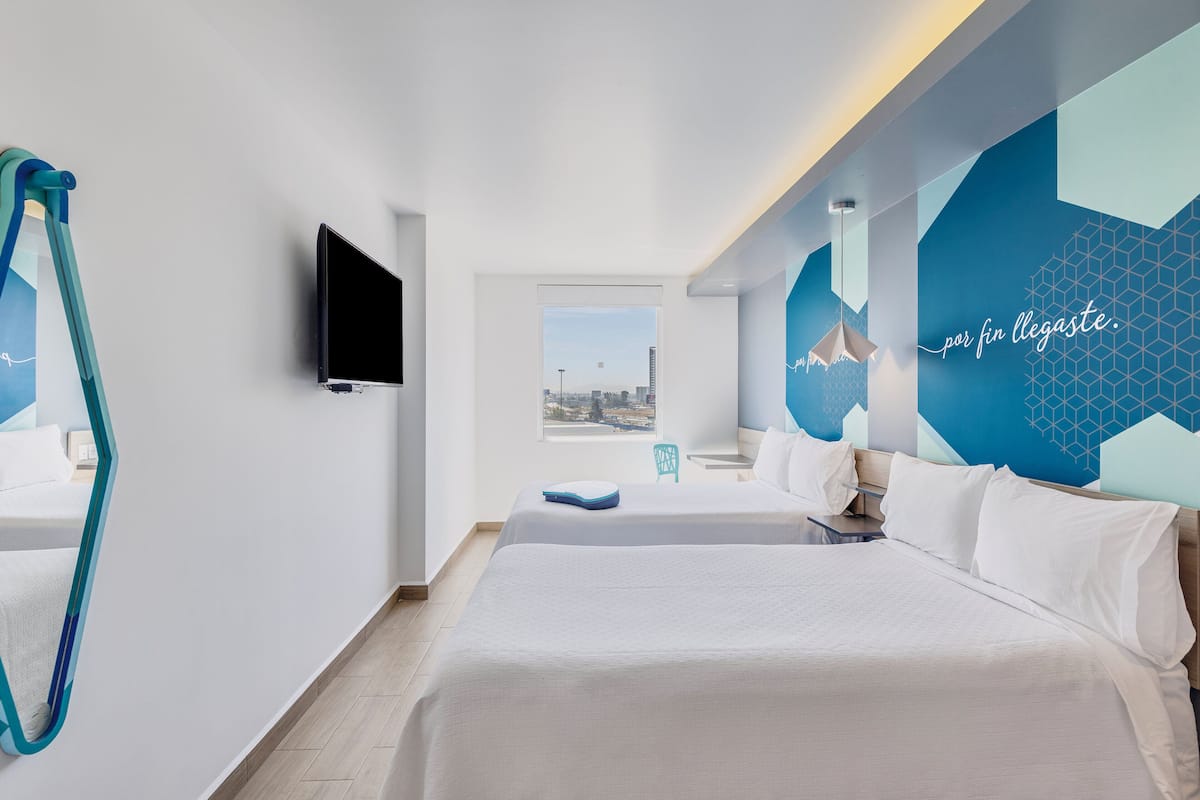 Una habitación de hotel moderna con una cama grande, un televisor y vistas a la ciudad desde una ventana.