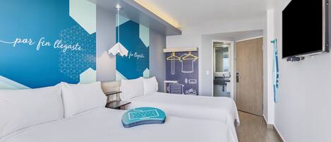 Una habitación de hotel moderna con una cama grande, un televisor montado en la pared y un diseño geométrico en la pared.