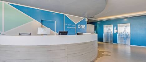 A reception desk with a modern design, a blue accent wall, and a sign that reads "Que gusta verde, bienvenido".
