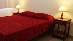 A neatly made bed with a red bedspread and pillows, flanked by two wooden nightstands with lamps. - Hotel Universal (Mendoza)