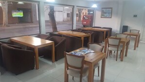A restaurant with wooden tables and chairs, large windows with a view of the street, and a red vehicle outside. - Hotel Universal (Mendoza)