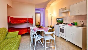 Une pièce compacte comprenant des lits superposés, un coin cuisine, un espace repas avec une table et des chaises, et un canapé.