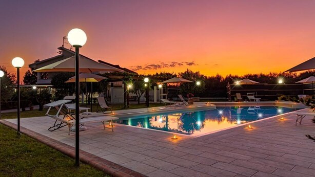Une piscine entourée d’une terrasse dallée, avec des chaises longues et des parasols.