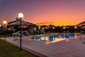 A swimming pool with lounge chairs and umbrellas, surrounded by a paved patio area. - Country House Jamm Jà (Capaccio-Paestum)