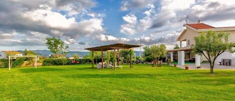 A spacious outdoor area with a wooden pergola, a well-maintained lawn, and a building with a red roof.