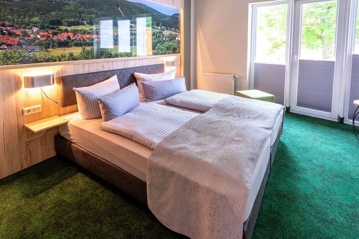 A bedroom with a bed, bedside tables, a view of a village through a window, and a radiator.