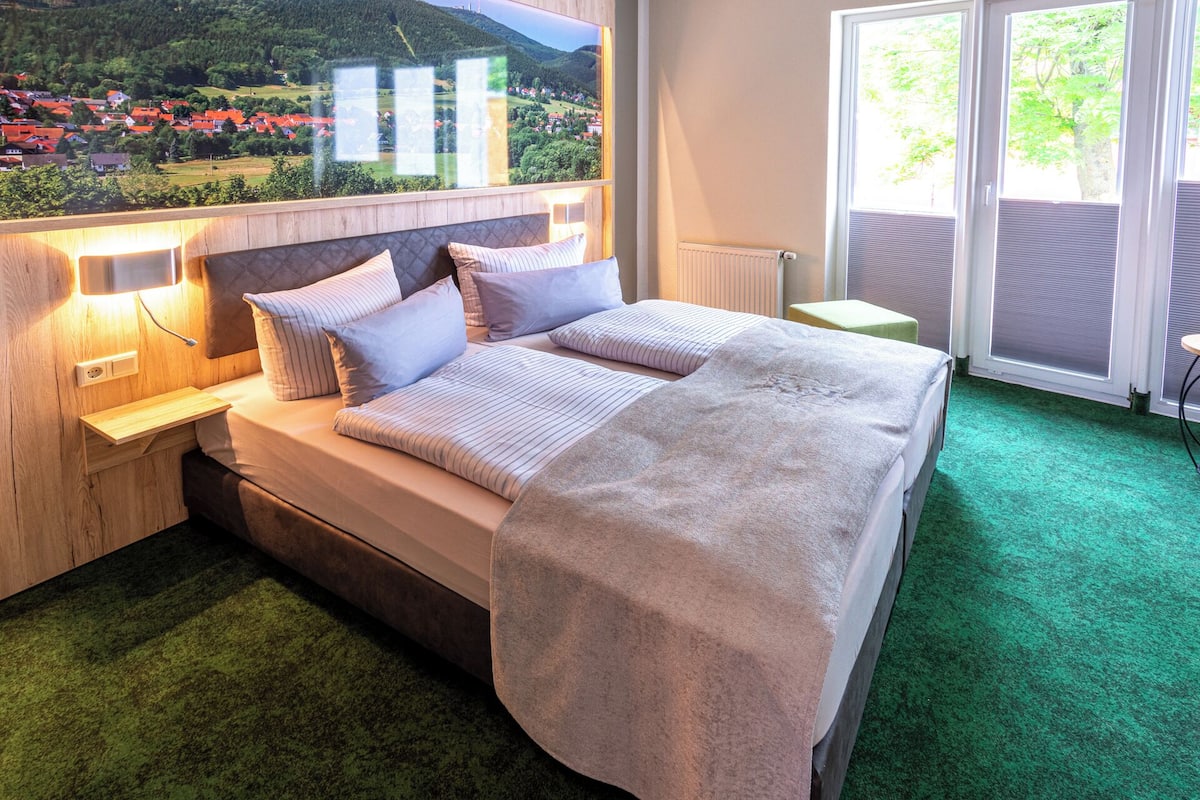 A bedroom with a large bed, wooden headboard, and a view of a village through a window.