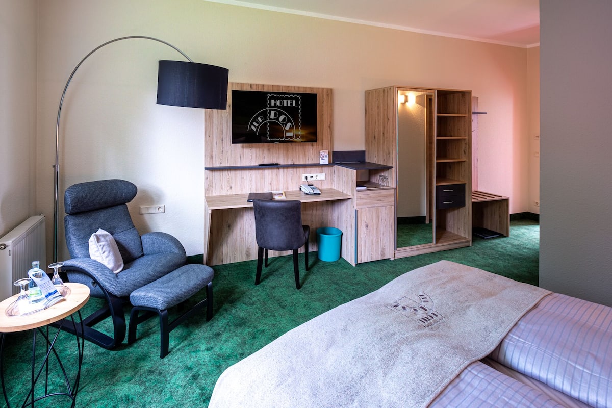 A hotel room with a bed, a desk with a computer, a chair, a TV, and a wardrobe.