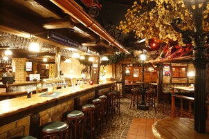 A bar area with wooden stools, a counter with glasses, and a sign indicating 'Friedhofstraße'.