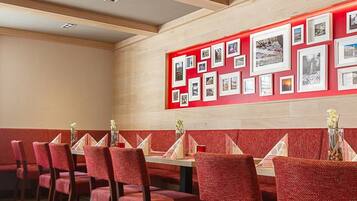 Een restaurant met rode bekleden stoelen en een muur versierd met ingelijste foto’s.
